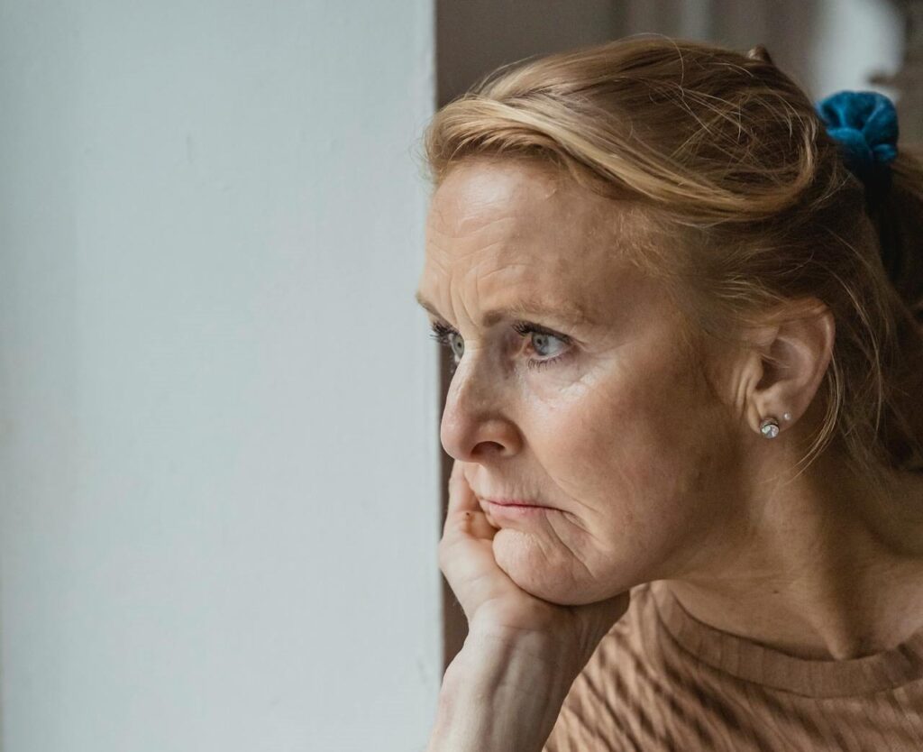 Zamyślona kobieta patrząca w okno – overthinking i jego wpływ na zdrowie psychiczne i hormonalne